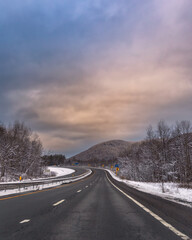 Fototapeta premium Isolated empty highway surrounded by wintery snow scene under a colorful stormy sky. Upstate New York