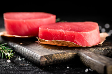 Raw tuna steaks on a rosemary cutting board. 