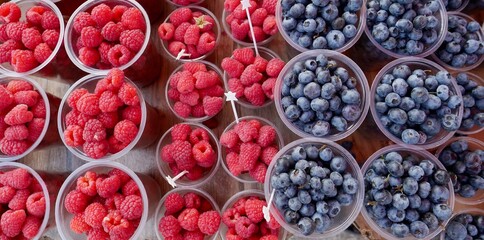 Aerial view of fresh raspberries and blueberries in plastic cups for sale.