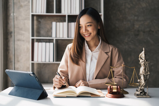 Attractive young lawyer in office Business woman and lawyers discussing contract papers with brass scale on wooden desk in office. Law, legal services, advice, Justice and real estate concept.
