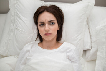 Unhappy young woman lying in bed at home, copy space