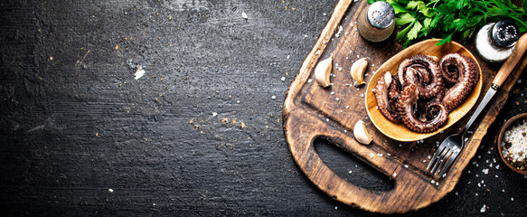 Fresh octopus on a plate on a cutting board with herbs and spices.