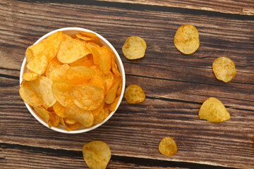 Crispy chips in a white cup. Junk food on a brown background.