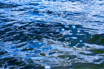 High shutter speed closeup shot of a wavy lake water flow. Deep blue black colors of the lake water surface.