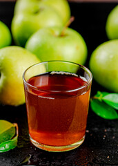 A glass of green apple juice with leaves on the table. 