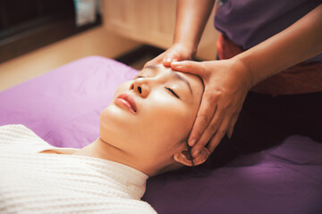 Fototapeta na wymiar Asian woman receiving a facial massage at an aesthetic salon. Beautiful young woman enjoying massage in spa salon. Girl facial treatment and skin care. Facial beauty treatment. Cosmetology.