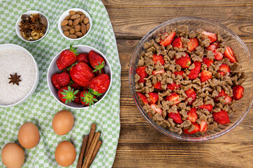 Tasty strawberry homemade crumble preparation on rustic wooden table, top view. 