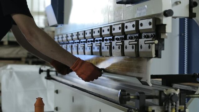 Experienced Craftsman In Black Jumpsuit And Orange Gloves Bends Aluminium Section Detail On Special Automatic Machine In Workshop