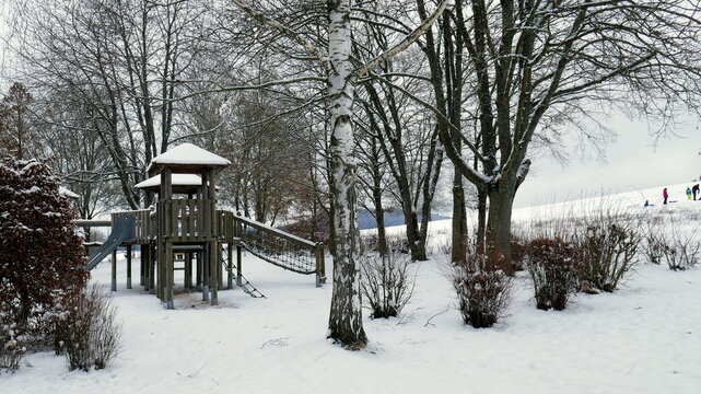 verlassener Spielplatz im Winter unter verschneiten Bäumen an kaltem nebeligen Tag