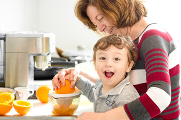 Child preparing orange juice in the kitchen with his grandmother