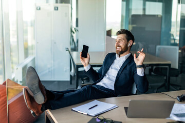 Rest and relax concept. Happy middle aged businessman enjoying music in earphones, sitting at desk with feet on table