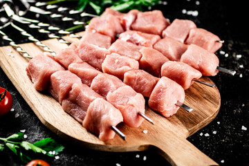 Pork kebab raw on a cutting board with tomatoes and parsley. 