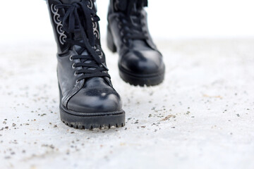 Female legs in black leather lace-up boots on a snow covered with anti-ice mixture. Woman walking on winter street, slippery in cold weather