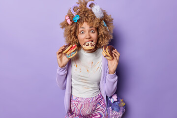 Food to avoid during pregnancy. Surprised woman with different items in head holds delicious doughnuts enjoys sweet desserts wears dirty t shirt sweatshirt carries net bag with toys for future baby