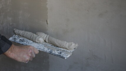 a plasterer's hand with a wide spatula and a thick elastic mortar putty and level the wall and copy...