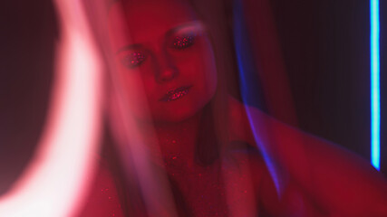 Color glow girl. Nightclub look. Disco fashion. Blur red neon light woman with shimmering face skin...