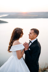 Portrait of happy bride in luxury dress and groom embracing in front of big lake