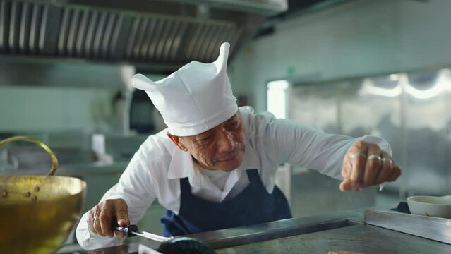 Professional senior male chef in a hat makes final touches on a freshly made food before serving.