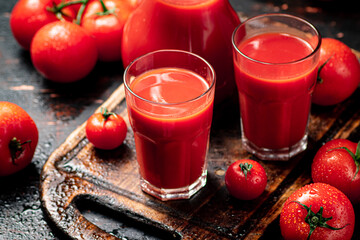 Tomato juice in glasses on a wooden cutting board. 