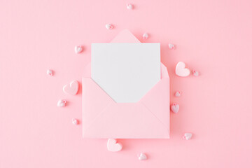 Valentines Day concept. Flat lay photo of open envelope with white card and hearts on pastel pink background. Lovers holiday card idea.