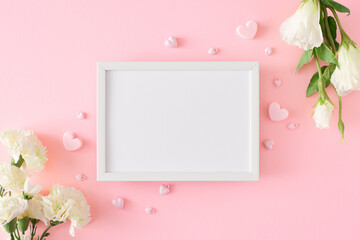 Hello spring concept. Flat lay photo of white spring flowers and hearts on pastel pink background and frame in the middle. 8-march holiday card idea.