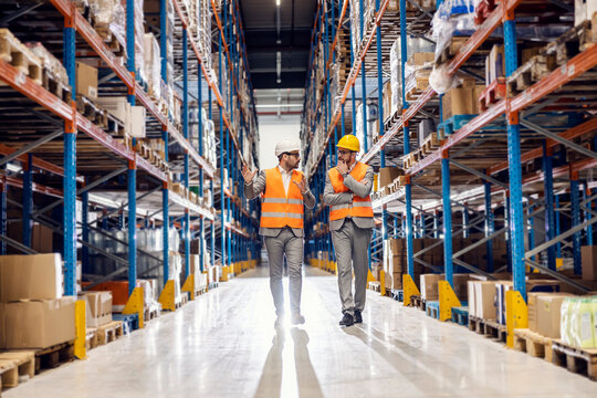 A manager walking through warehouse with businessman and explaining logistics.