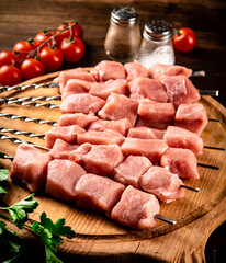 Pork kebab raw on skewers with parsley and tomatoes on a cutting board. 