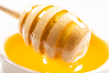 Liquid natural bee honey in a white ceramic bowl with a wooden spoon.