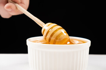 Honey in a white ceramic bowl with a wooden spoon on a black background.