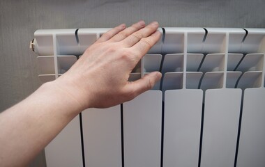 A man's hand touches a white bimetallic radiator in an apartment