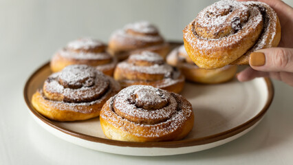 Freshly baked cinnamon rolls sprinkled with powdered sugar on parchment paper. Sweet homemade Christmas baking. . Kanelbule is a Swedish dessert.