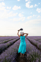 Rear view of woman in hat holding a bouquet of lavender flowers on the field