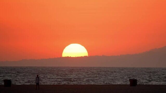 Magical huge sunset with the sun being half way behind the horizon in front of a blood orange sky at the Santa Monica in Los Angeles, USA.