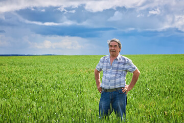 Naklejka na ściany i meble Portrait of a happy farmer kneeling down in a wheat field with a beautiful landscape in the background