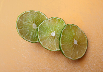 Persian lime fruit slices on an orange cutting board. Lime is a citrus fruit. This lime is a cross...