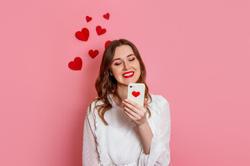 The girl reads love sms smiling on a pink background. valentine's day congratulations