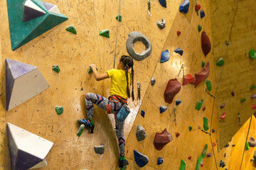 bouldering, little girl climbing up the wall and climber multicolored grips. Leisure activity