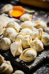 Raw dumplings on a cutting board with egg and flour. 