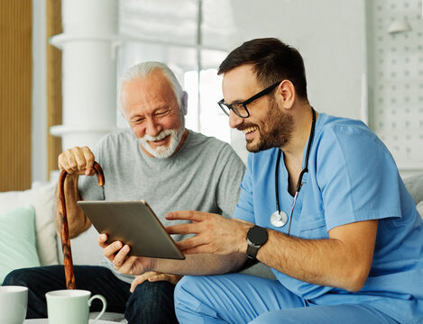 nurse doctor senior care tablet computer technology showing caregiver help assistence retirement home nursing elderly happy laughing man