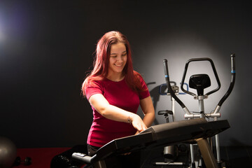 Fototapeta na wymiar A young woman in the gym is adjusting the treadmill