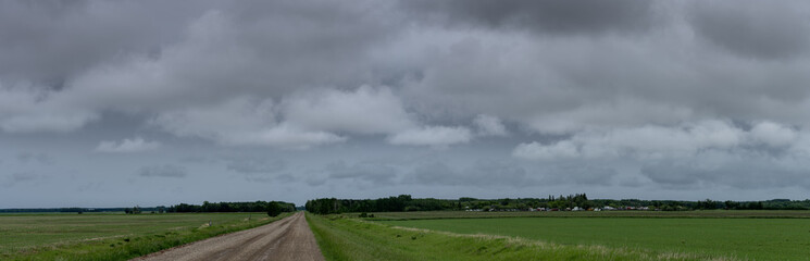 Obraz na płótnie Canvas View down a dirt farm country road surrounded by green fields and under a sky full of gray storm clouds. 