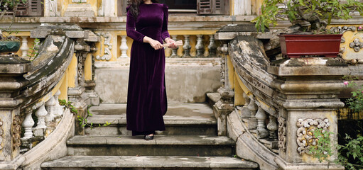 Vietnamese lady in purple velvet Ao Dai, standing elegantly at an ancient building