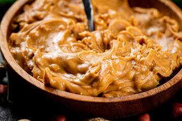 A wooden plate of peanut butter with a spoon. 