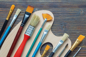 Different types of paintbrushes ( round, flat, angular, comb, detail, fan ) and palette on dark...