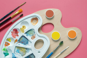 Obraz premium Watercolor paints, paintbrushes and palette on pink background. Copy space