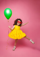 Portrait of a cheerful little girl isolated on a pink background, holding a bunch of colorful balloons, posing.