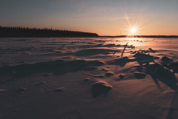 The sun at sunset illuminates the ice on the Vilyui River in Yakutia in winter against the backdrop of a taiga forest with houses in the village of Suntar.
