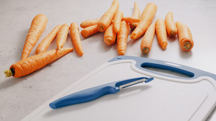 Fresh raw organic carrots,cutting board, and peeler knife close-up on a kitchen table