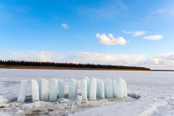 Cut ice with pillars for defrosting and eating stands covered with snow on the Vilyui River in Yakutia in winter against the backdrop of forest and clouds