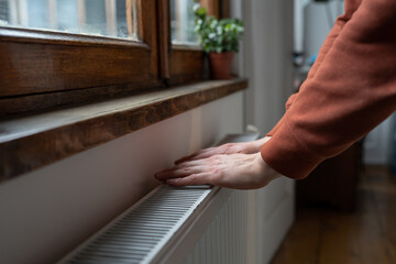 Closeup of man in sweater wants to keep warmth in apartment. Female puts hands on room central...